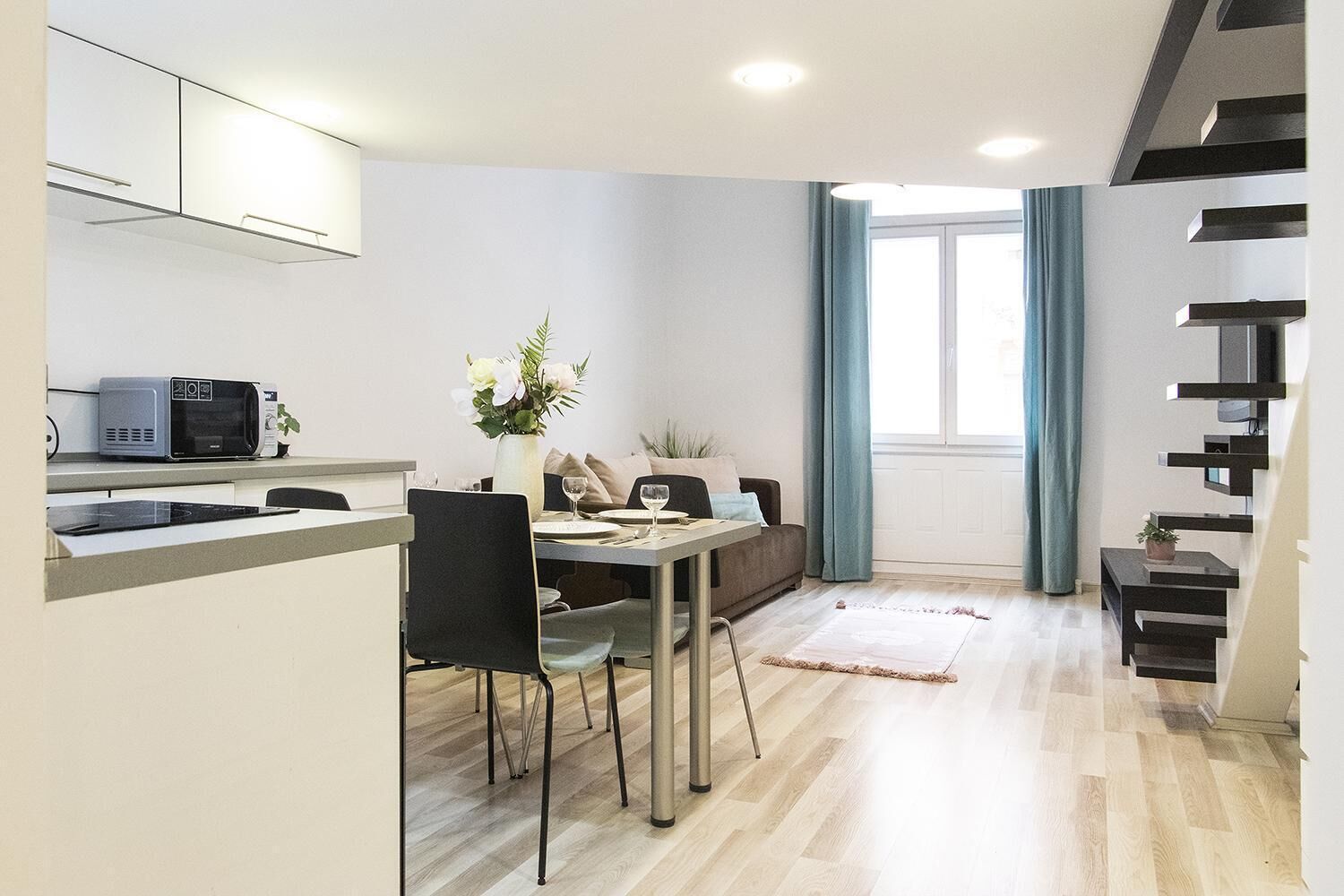 Un espacio habitable compacto con kitchenette, comedor y una escalera.