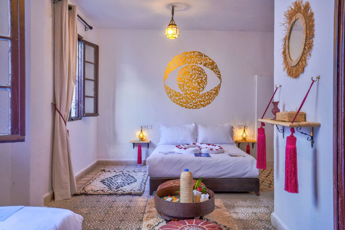 A bedroom with a bed, bedside tables, a decorative wall piece, a hanging light fixture, and a patterned rug.