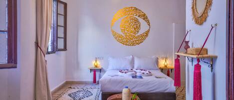 Un dormitorio con cama, mesitas de noche, un adorno en la pared, una lámpara colgante y una alfombra estampada.