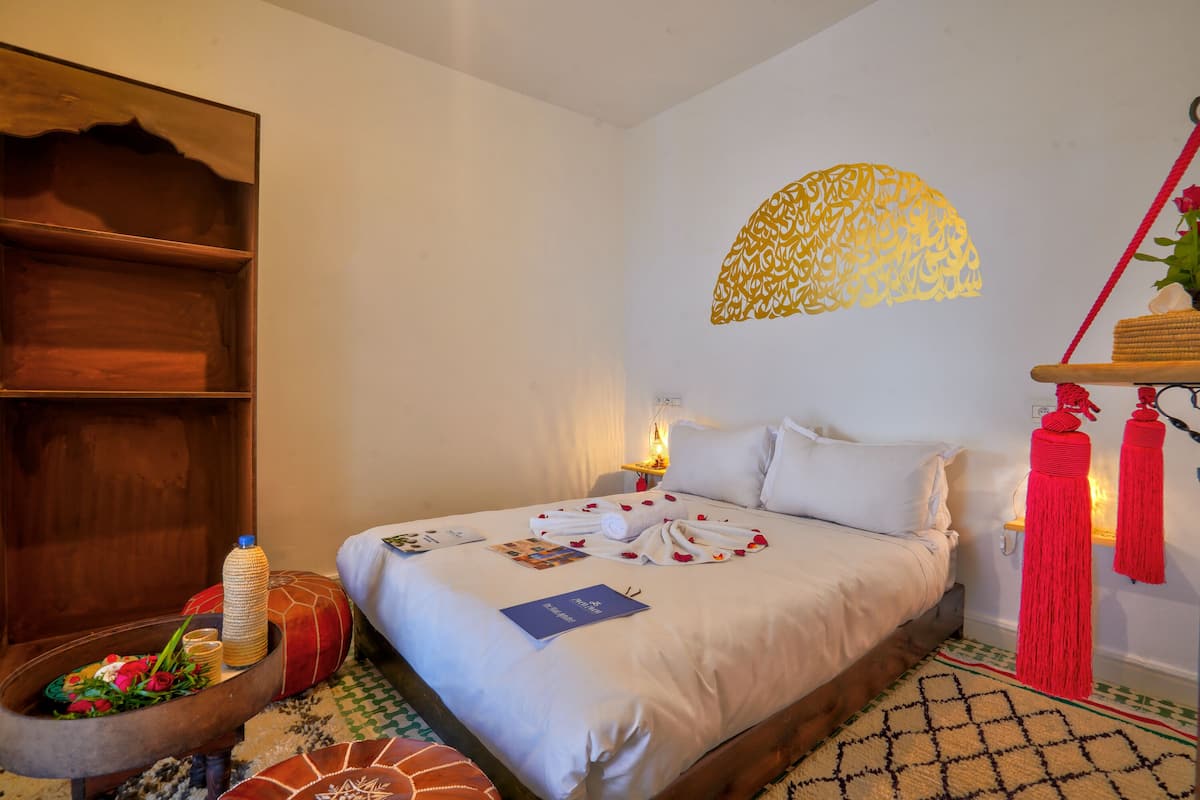 A neatly made bed with white linens, a wooden headboard, and a decorative wall hanging.