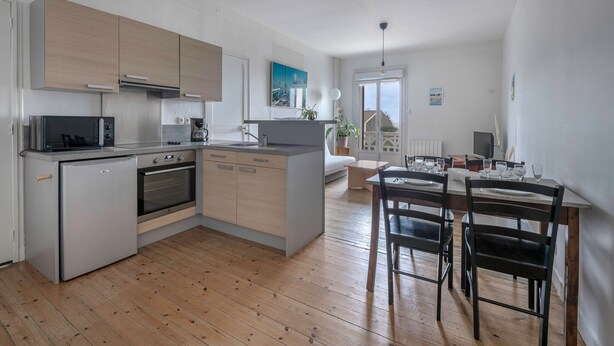 A modern kitchen with wooden cabinets, a built-in oven, and a dining area with a table and chairs.