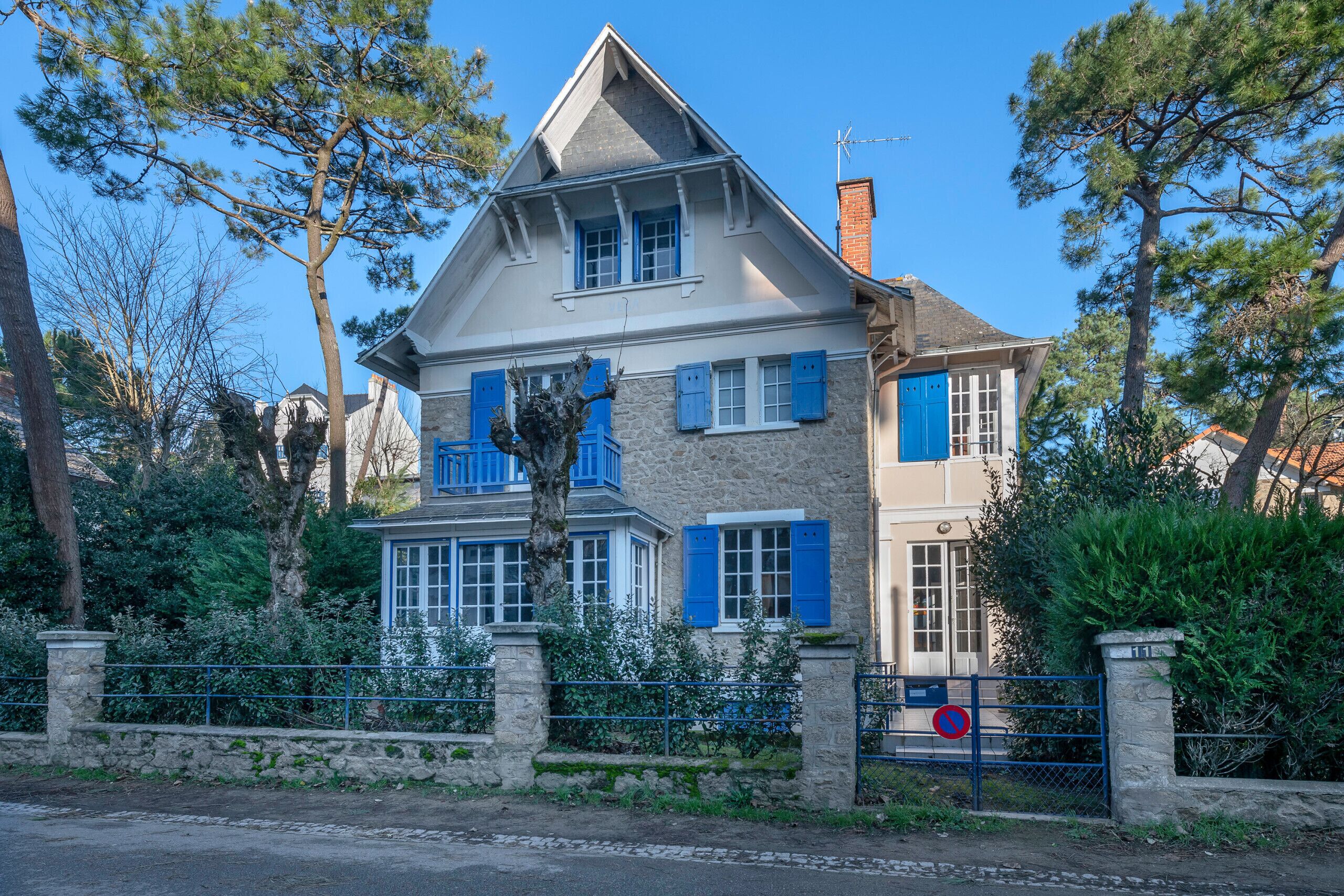 Una casa de dos pisos con contraventanas azules, fachada de piedra y portón de piedra.