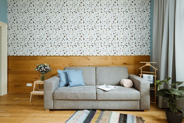 A modern living room with a grey sofa, a wooden headboard, a small side table with a vase of flowers, and a striped rug.