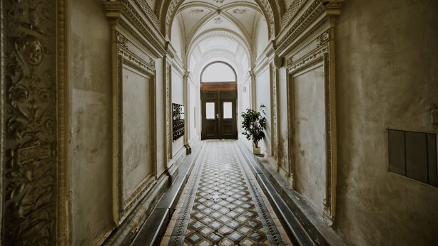 A corridor with ornate columns, a patterned floor, and a door at the end.