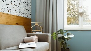 A modern living room with a grey sofa, a wooden hanger, a potted plant, and a window with curtains.