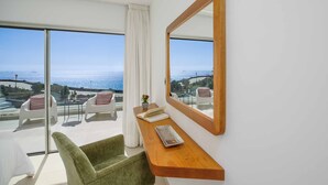 Ein modernes Zimmer mit großem Fenster zum Meer, einem Holztisch, einem grünen Stuhl und einem Spiegel an der Wand.