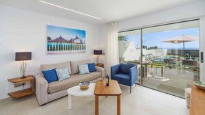 Ein modernes Wohnzimmer mit einer Couch, einem blauen Sessel, einem Couchtisch und einer Glastür zu einem Außenbereich mit Pool und Sonnenschirmen.