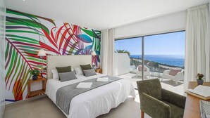 Ein modernes Hotelzimmer mit einem großen Bett, Meerblick und einem farbenfrohen, abstrakten Wandbild.