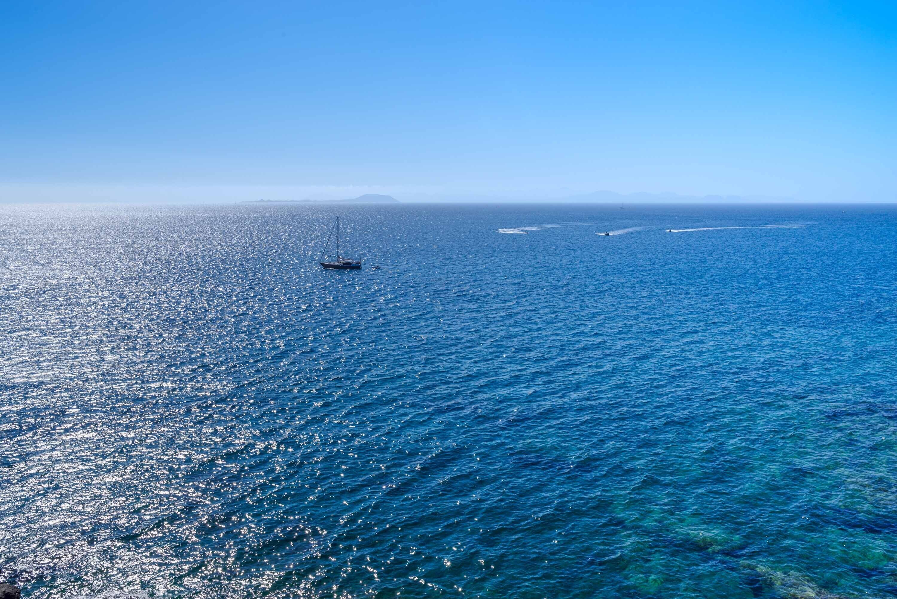 A clear view of a calm sea with a sailboat and distant land.