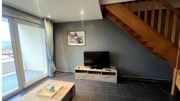 Uma sala de estar moderna com uma janela grande, uma escada de madeira e uma TV de tela plana sobre um suporte de madeira.