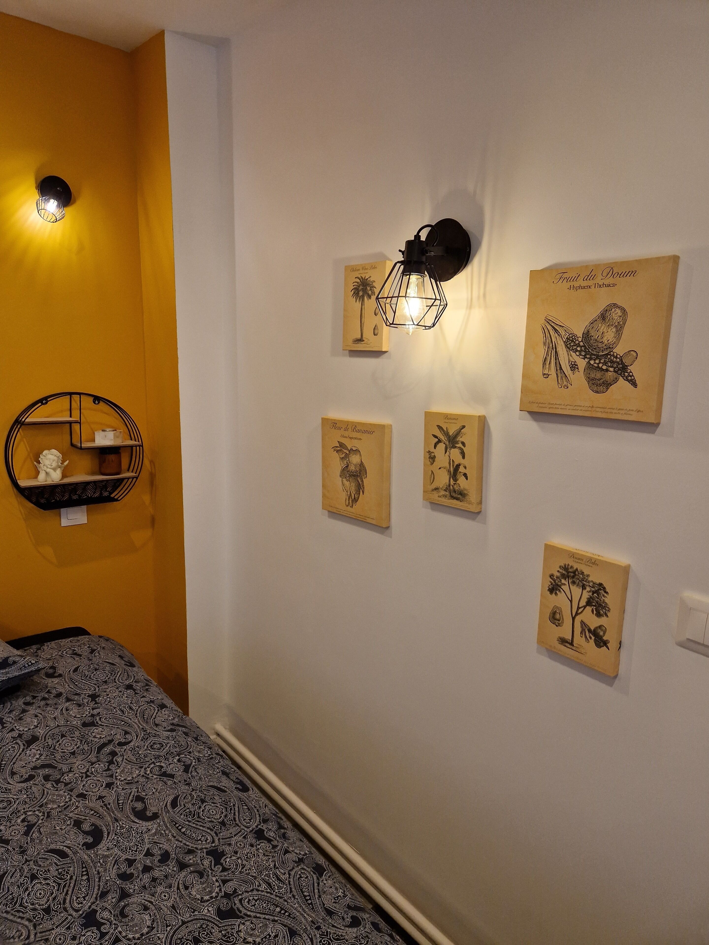 A room with a bed, a wall-mounted shelf with decorative items, and four framed botanical illustrations.