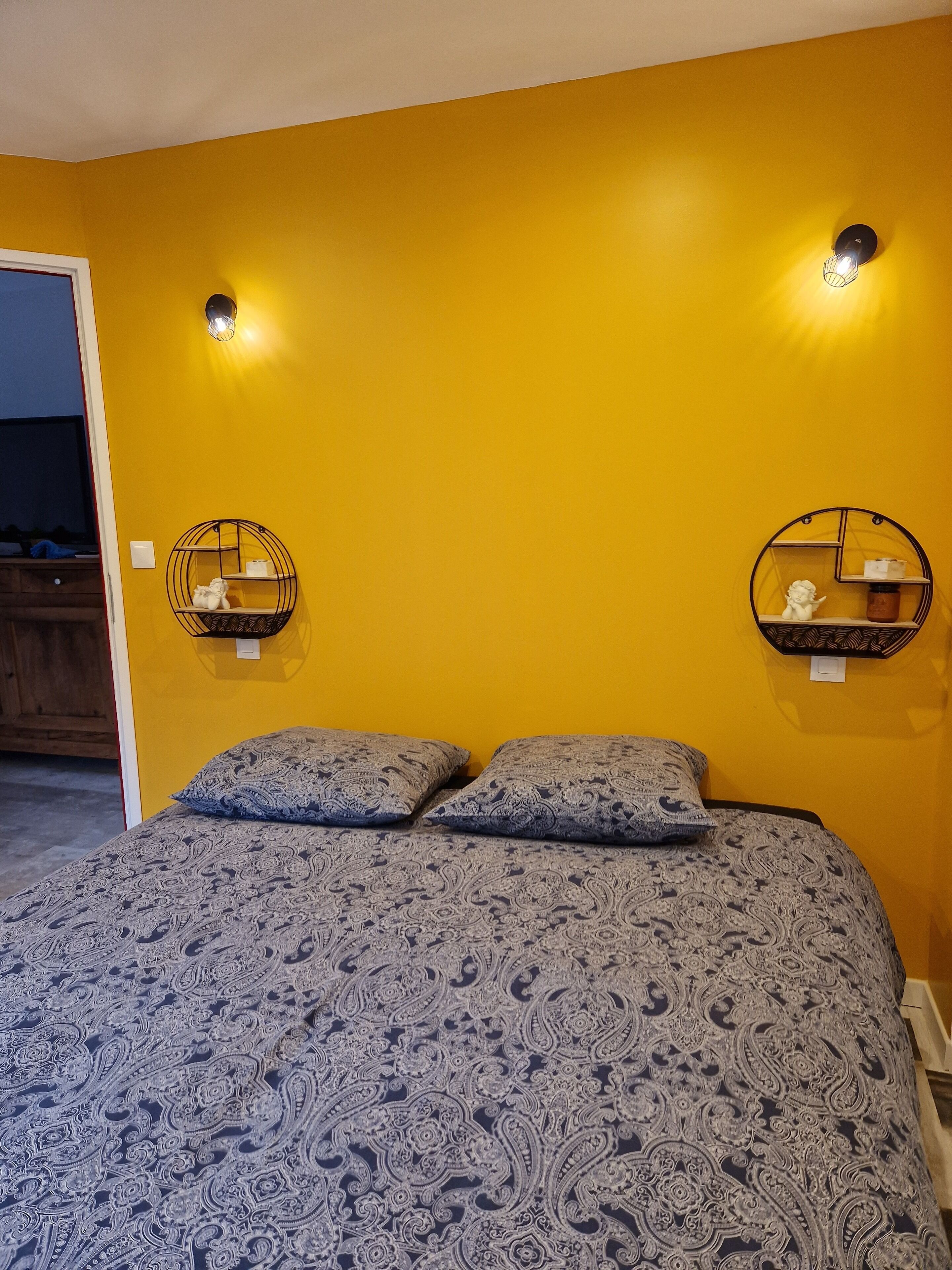 A bedroom with a bed, two wall-mounted shelves, and a door.
