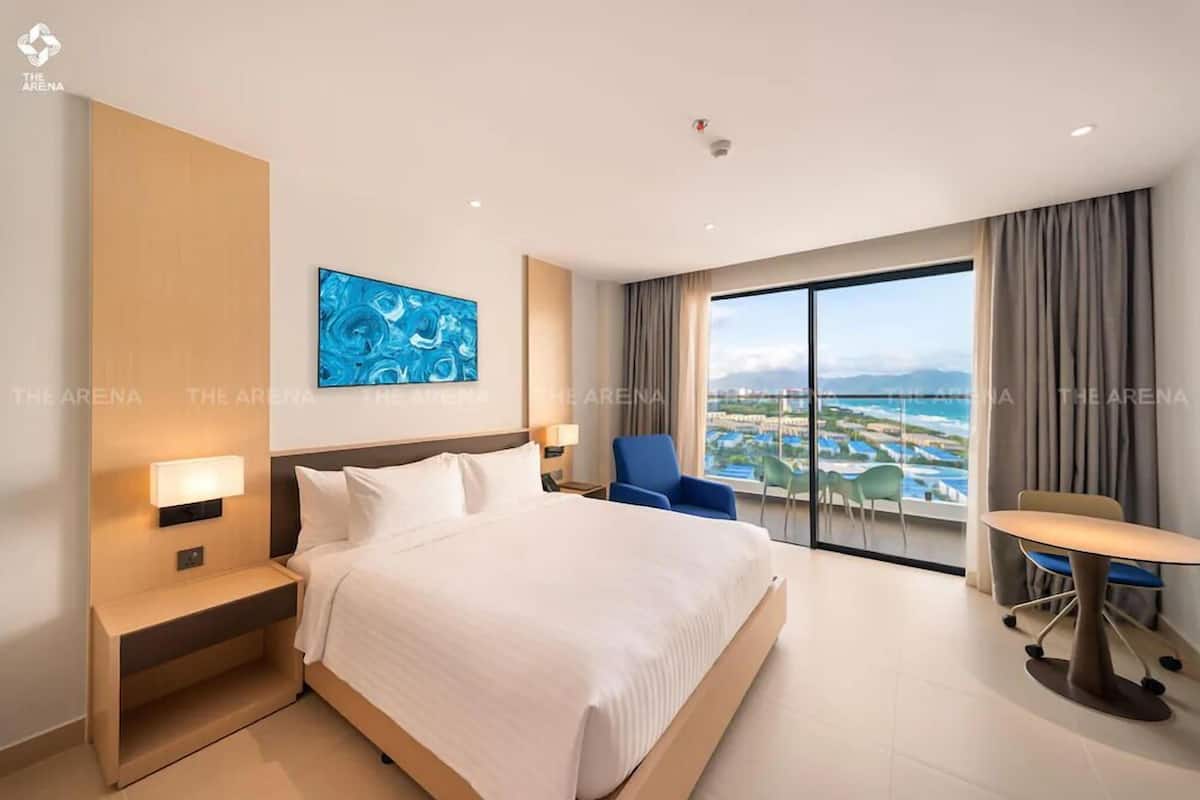 A modern hotel room with a large bed, a desk, and a view of a coastal area.