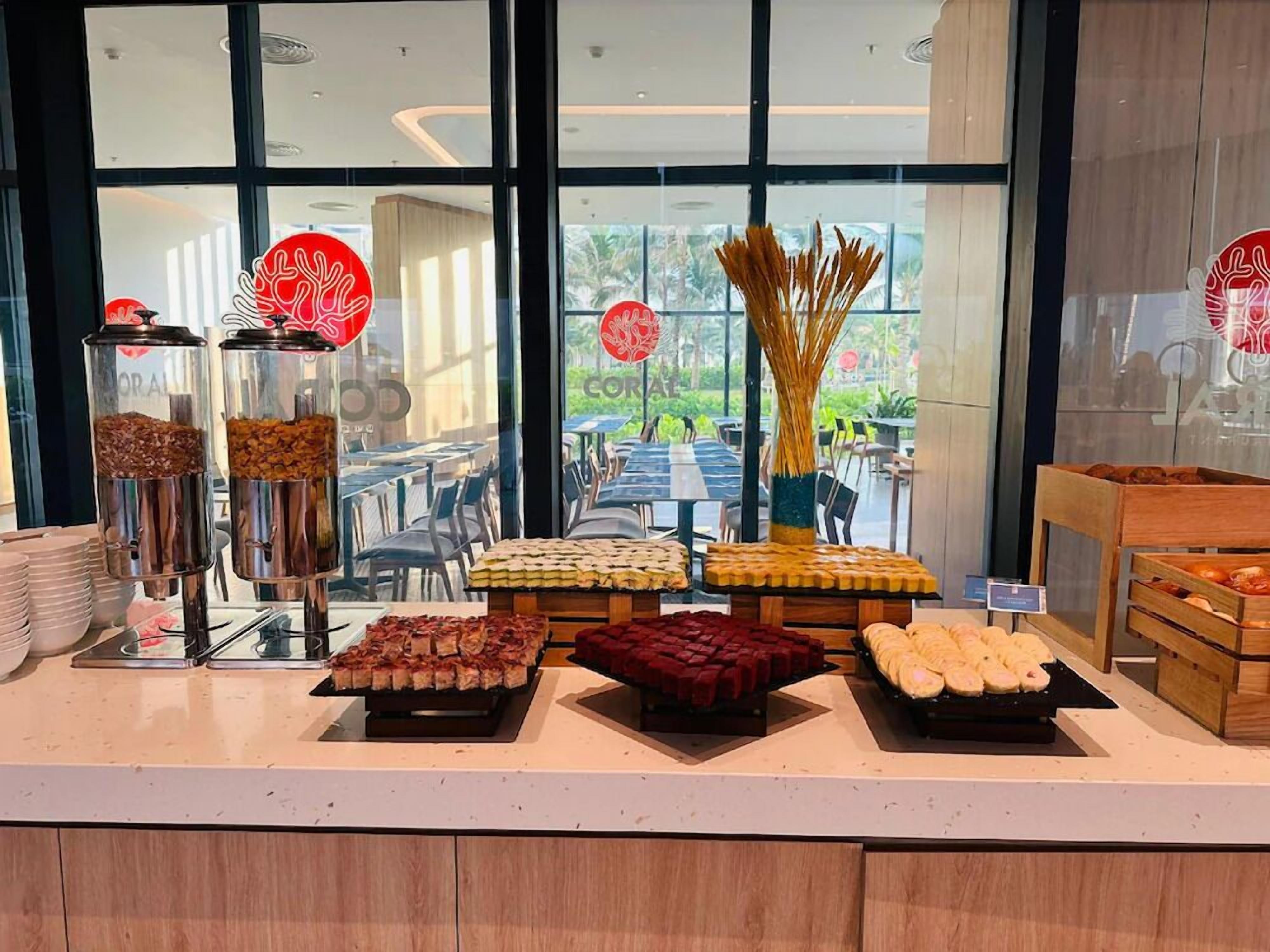 A buffet area with various food items displayed on trays and in containers, with a view of outdoor seating and greenery in the background.