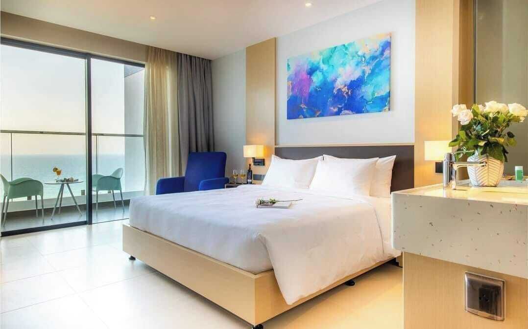 Een moderne hotelkamer met een groot bed, uitzicht op zee, een blauwe stoel en een schilderij aan de muur.