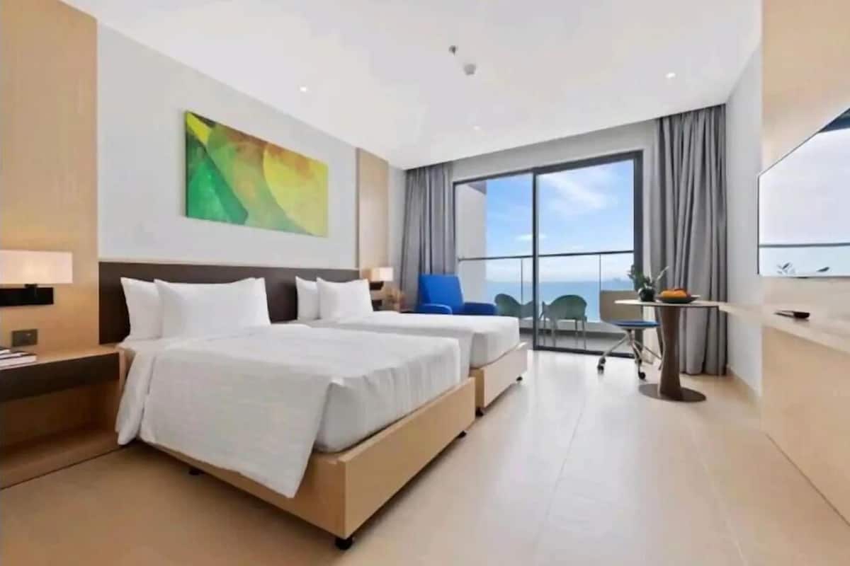 A modern hotel room with two beds, a desk, a chair, and a large window offering a view.