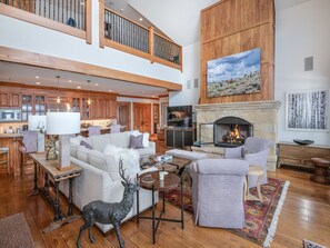 A spacious living area with a fireplace, a high ceiling, and a kitchen in the background. - Horizon Pass | Luxury 5BR Ski-In/Ski-Out, Heated Pool (Edwards)