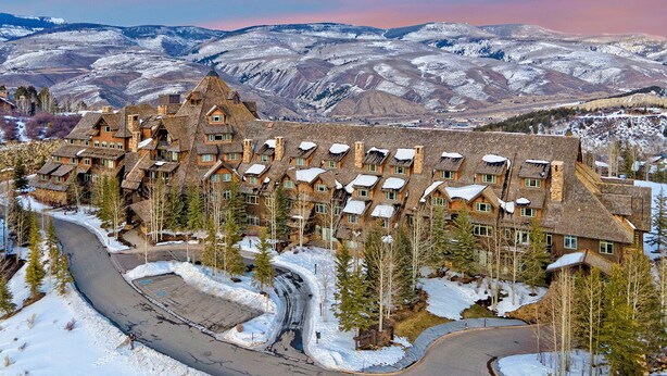 A large, multi-story lodge with a unique architectural design, surrounded by snow-covered mountains and a winding road.