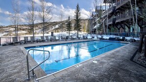 A swimming pool with lounge chairs and a stone deck, surrounded by trees and a building with balconies.