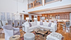 A spacious living room with a large sectional sofa, a coffee table, and a dining area with wooden cabinets and a kitchen in the background.
