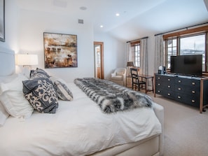 A modern hotel room with a large bed, a desk, a television, and a painting on the wall. - Horizon Pass | Luxury 5BR Ski-In/Ski-Out, Heated Pool (Edwards)