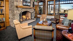 A cozy living room with a stone fireplace, comfortable seating, and large windows offering a view of the outdoors.