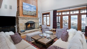 A cozy living room with a stone fireplace, comfortable seating, and large windows offering a view of the mountains.