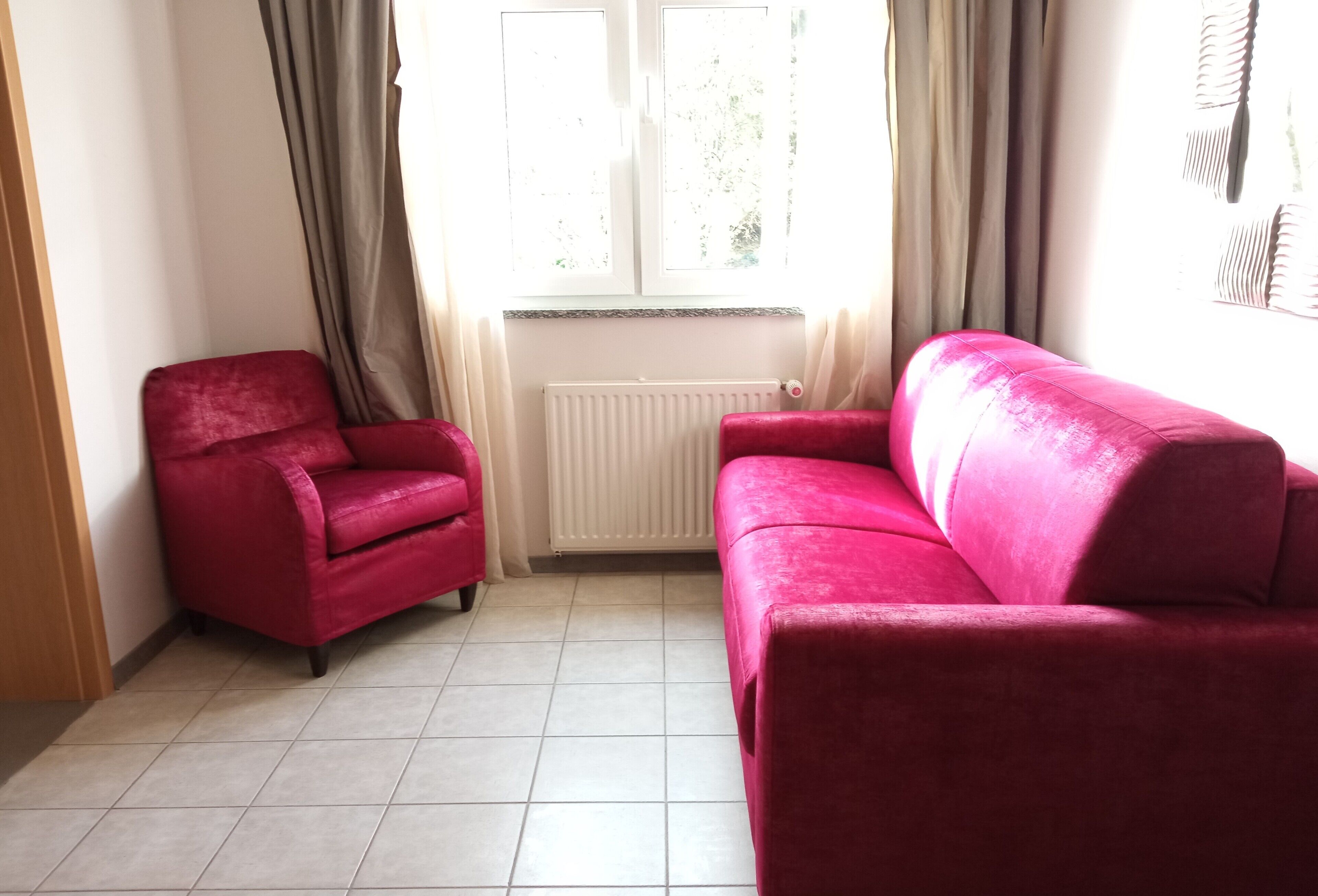 Una habitación con un sofá y un sillón rojos, un radiador y una ventana con cortinas.