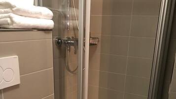 Une douche fermée par des parois de verre, avec des toilettes blanches et une serviette sur laquelle est brodé le nom « Hôtel Gründ ».