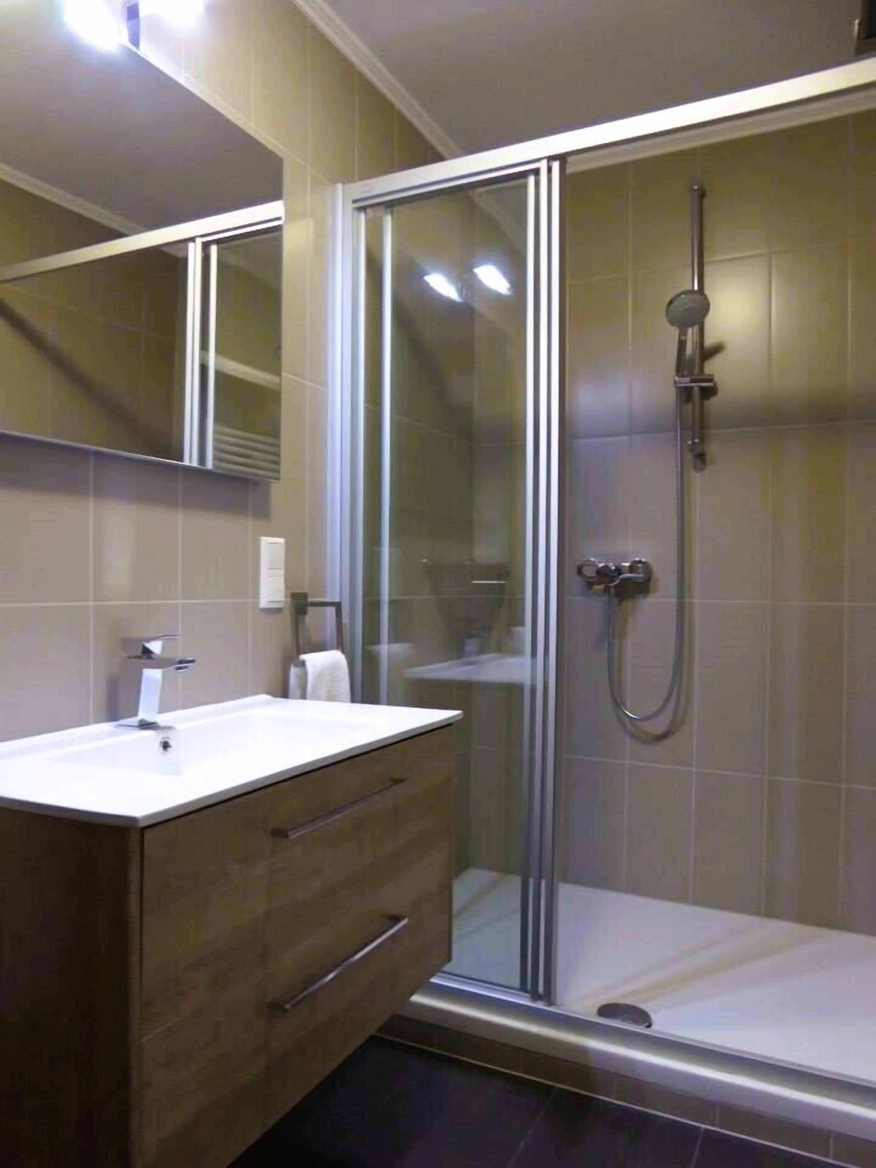 A modern bathroom with a glass-enclosed shower, a wooden vanity with a white sink, and a large mirror above the vanity.