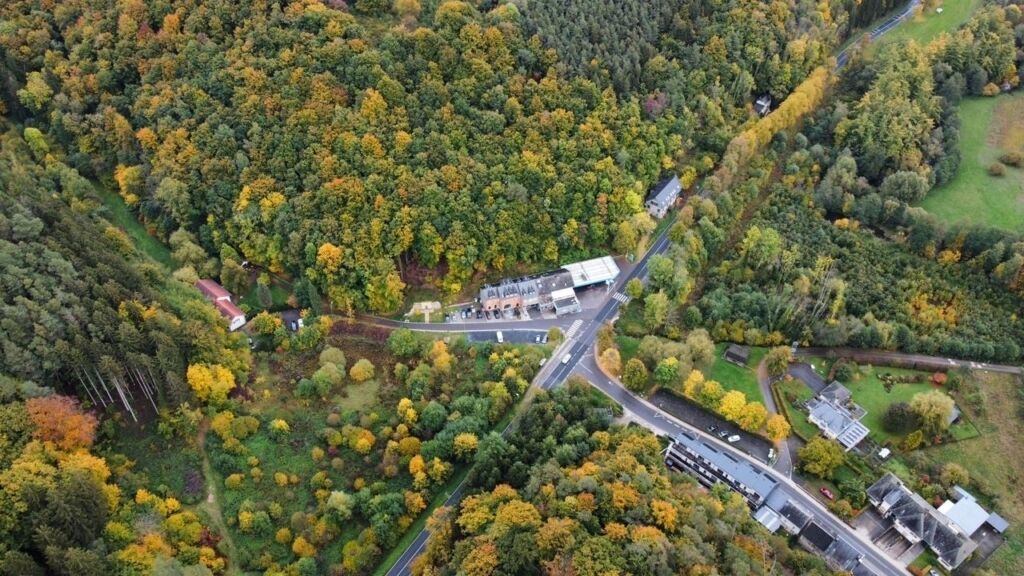Une vue aérienne d’une zone boisée avec une route, des bâtiments et un parking.