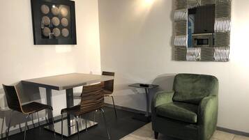 A modern living room with a dining table, two chairs, a green armchair, a small side table, and a decorative wall piece.