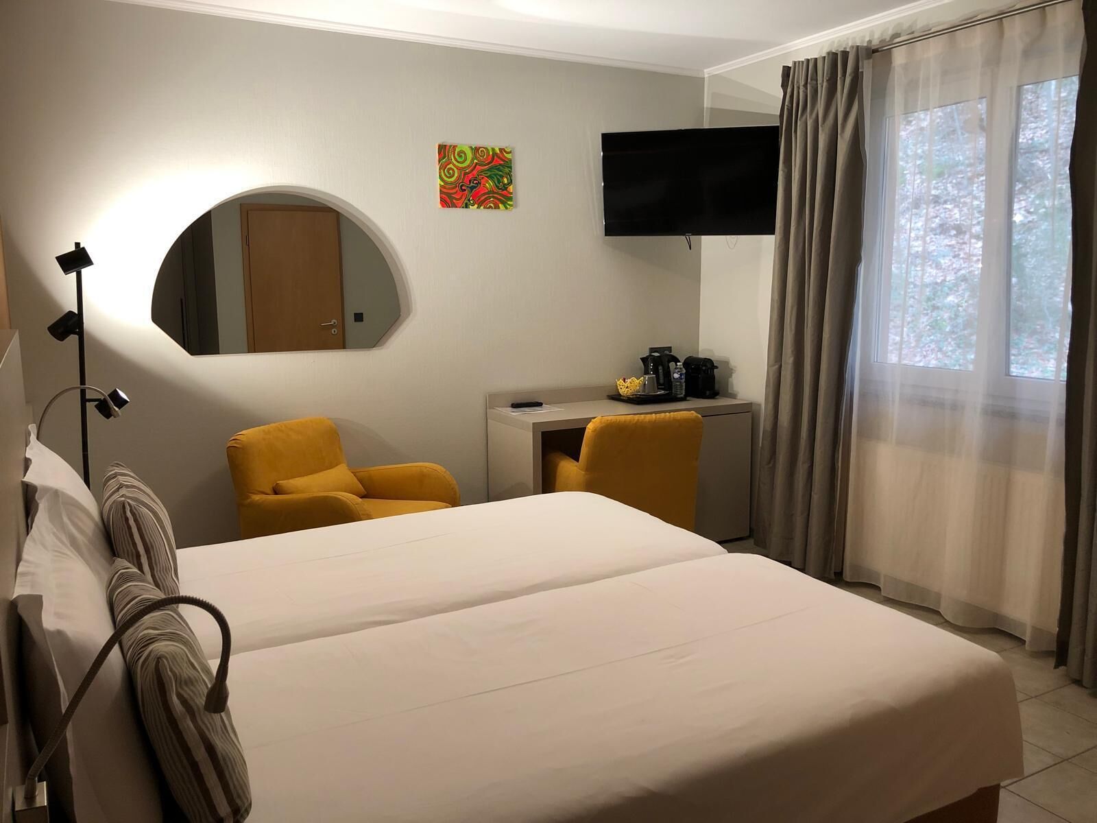 A hotel room with a bed, a desk, a chair, a TV, and a window with curtains.