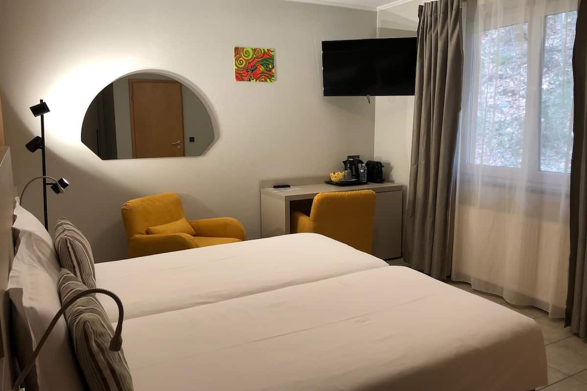 A hotel room with a bed, a desk, a chair, a TV, and a window with curtains.