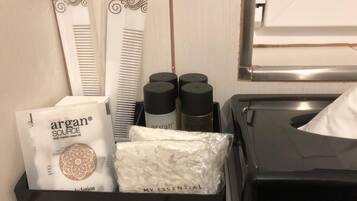 Servicios de la habitación de hotel, incluyendo un peine blanco, loción Argan Source y una bandeja negra con una caja de pañuelos.