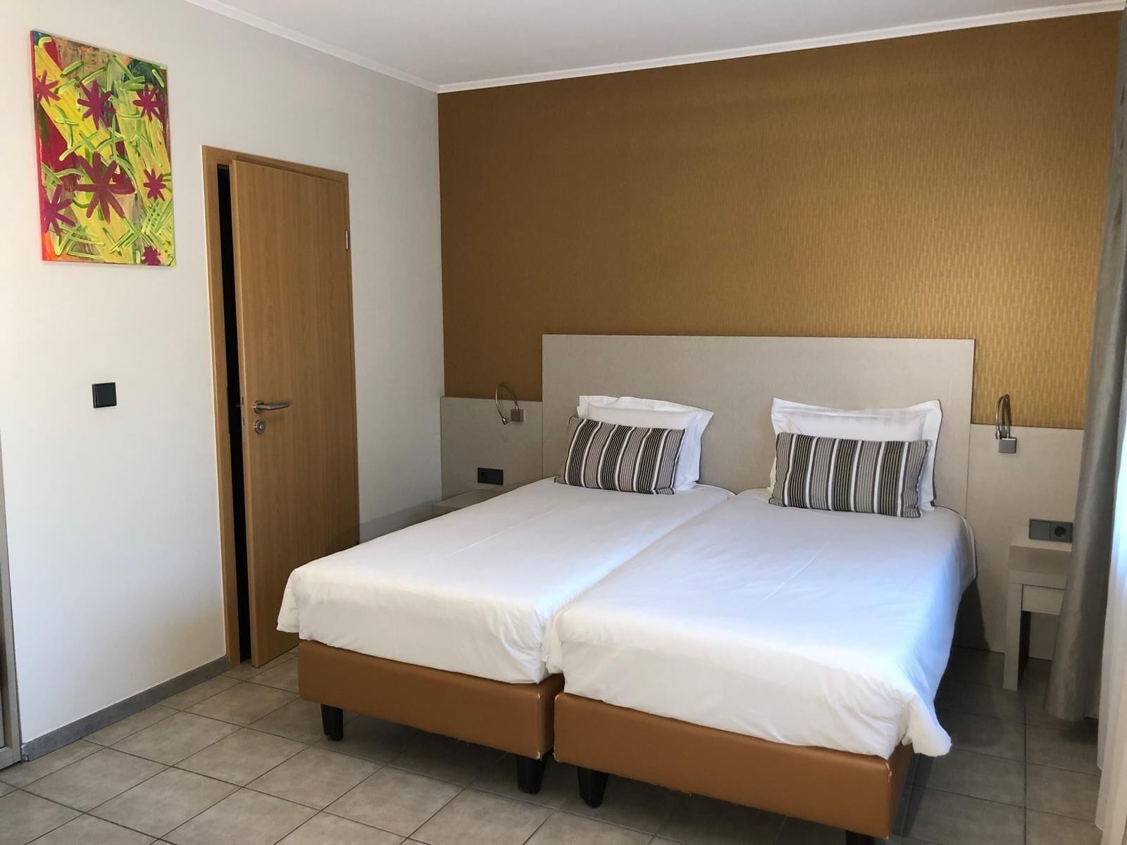 A double bed with two pillows, a wooden door, and a wall-mounted light fixture.