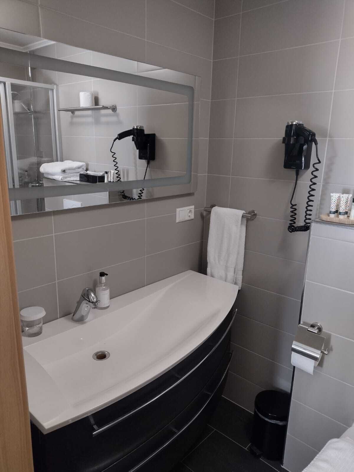 A bathroom with a white sink, a mirror, a towel rack, and a hairdryer mounted on the wall.