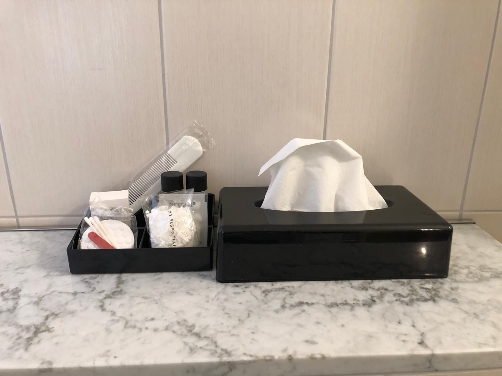 Un ripiano del bagno con un box di fazzoletti neri e un vassoio nero con articoli da toilette.