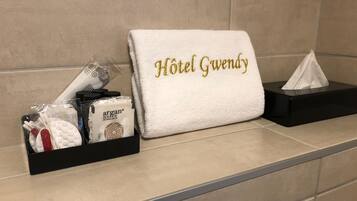 A hotel bathroom with a towel rack holding a white towel with "Hotel Gwen" embroidered in gold, a black tissue box, and a tray with toiletries.