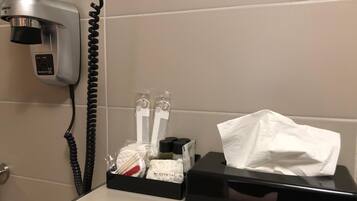 Une salle de bain équipée d’un sèche-cheveux, d’une boîte de mouchoirs et d’un contenant avec des articles de toilette.