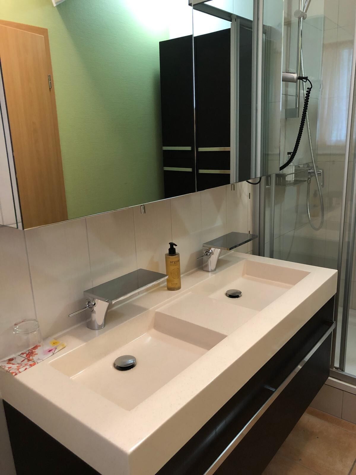 Un baño con un lavamanos grande y blanco, una cabina de ducha de vidrio y un espejo sobre el lavamanos.