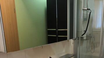 Un baño con un lavamanos grande y blanco, una cabina de ducha de vidrio y un espejo sobre el lavamanos.