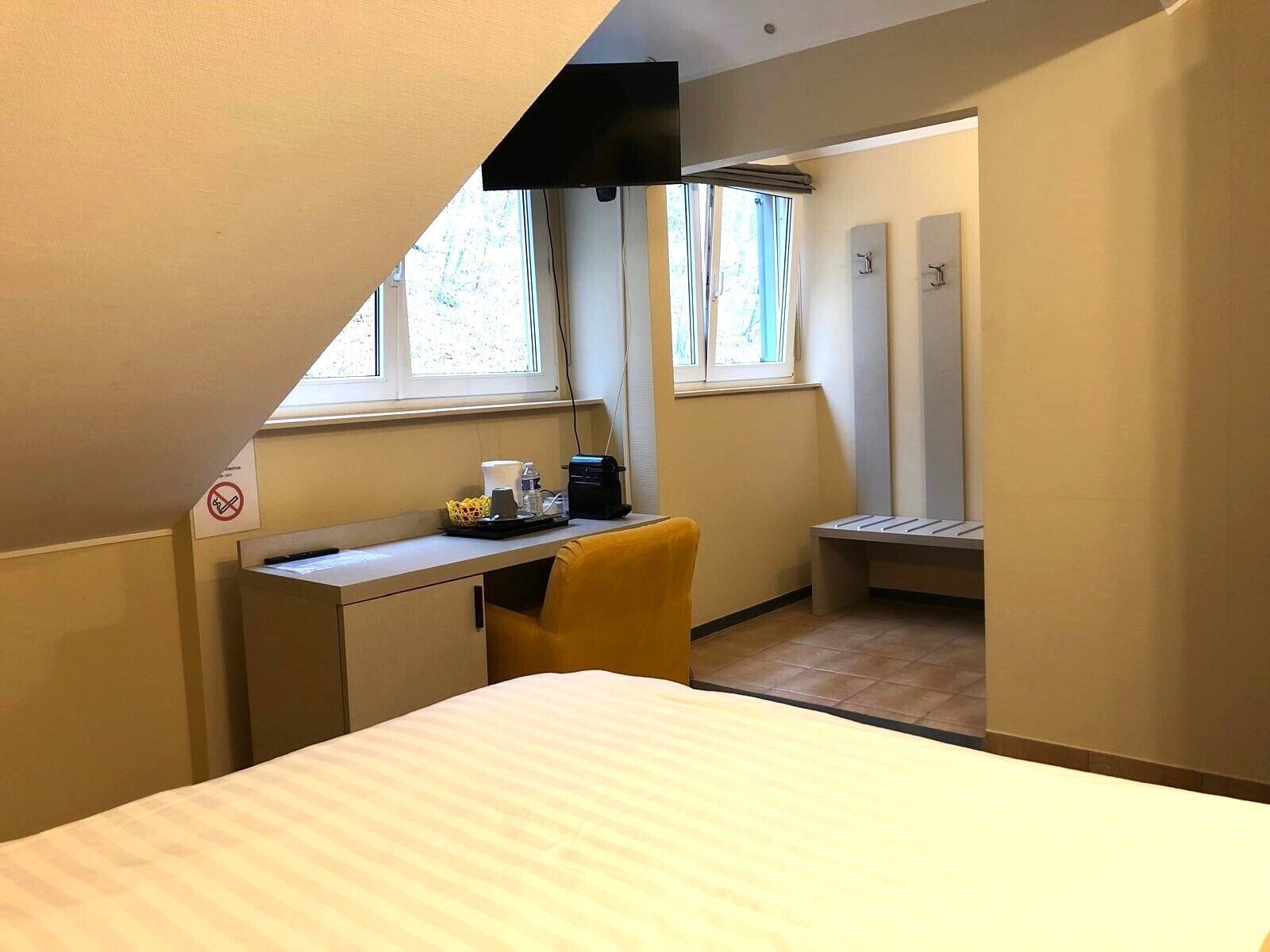 Una habitación de hotel compacta con una cama, un escritorio con cafetera, una silla y un banco.