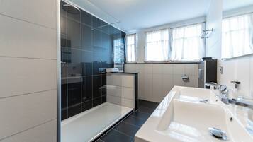 Un bany modern amb una cabina de dutxa de vidre, un lavabo blanc i un mirall.
