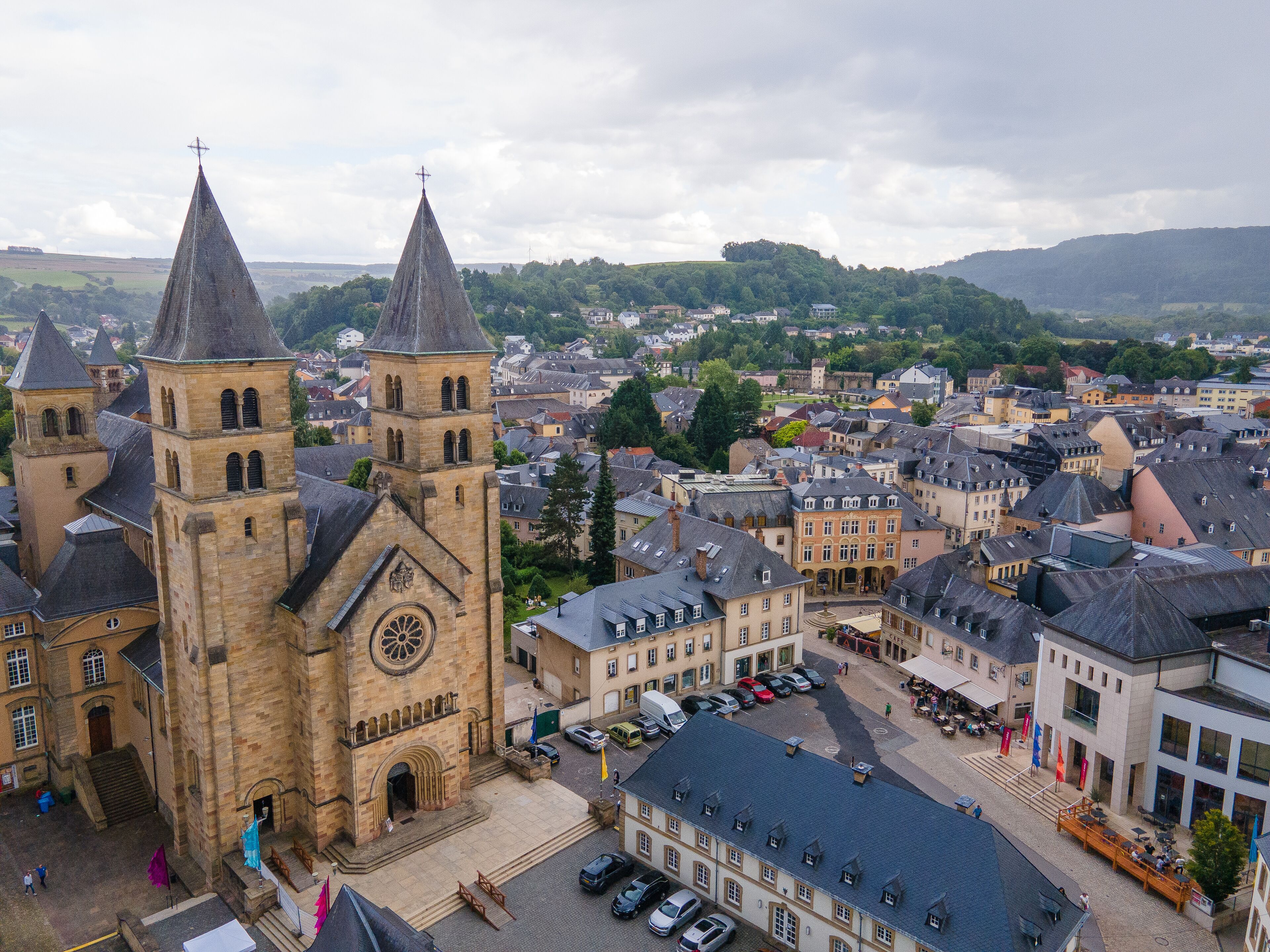 A historic church with two prominent towers and a large central tower, surrounded by a town with cobblestone streets and traditional buildings.