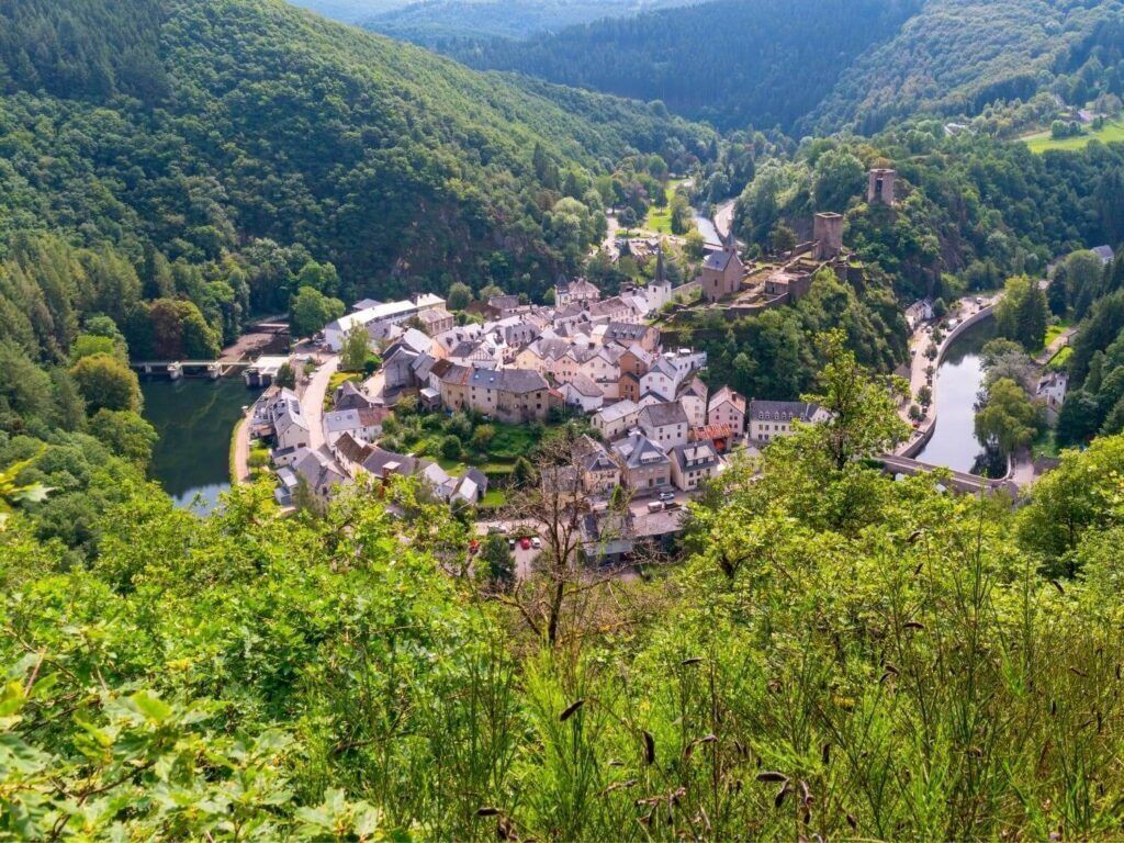 A historic town nestled in a valley with a river, surrounded by lush greenery and hills.