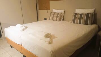 A neatly made bed with white linens and striped pillows, a rolled towel, and a wooden headboard.