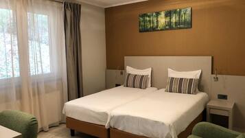 Habitación de hotel con cama doble, mesita de noche, una silla y un cuadro en la pared.