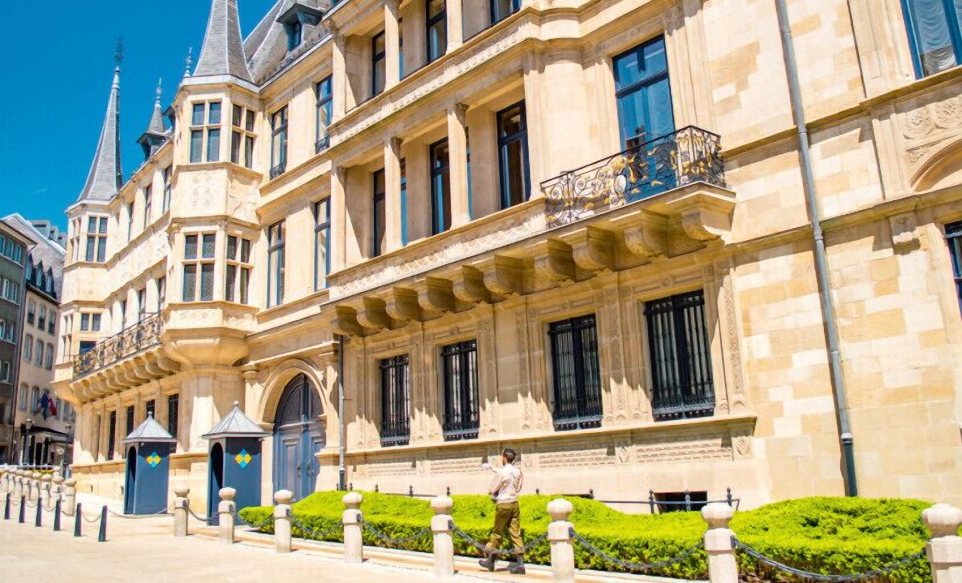 Un edificio histórico con arquitectura ornamentada, ventanas amplias y un jardín bien cuidado.