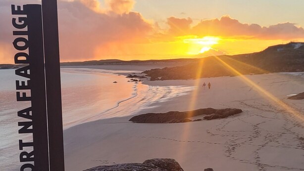 Eine Bank mit Blick auf einen Strand und einen Sonnenuntergang.